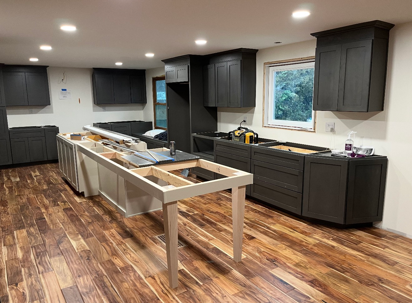 A kitchen undergoing renovation with dark cabinets, wooden floors, and a central unfinished wooden island frame.