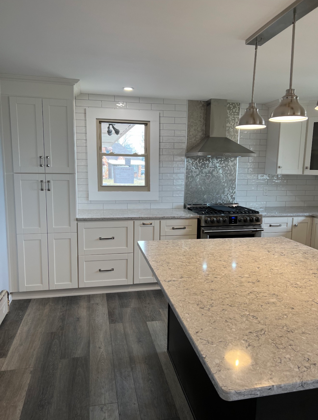 A bright, modern kitchen featuring white cabinets, a speckled stone island, gray wood floors, and a stainless steel stove.