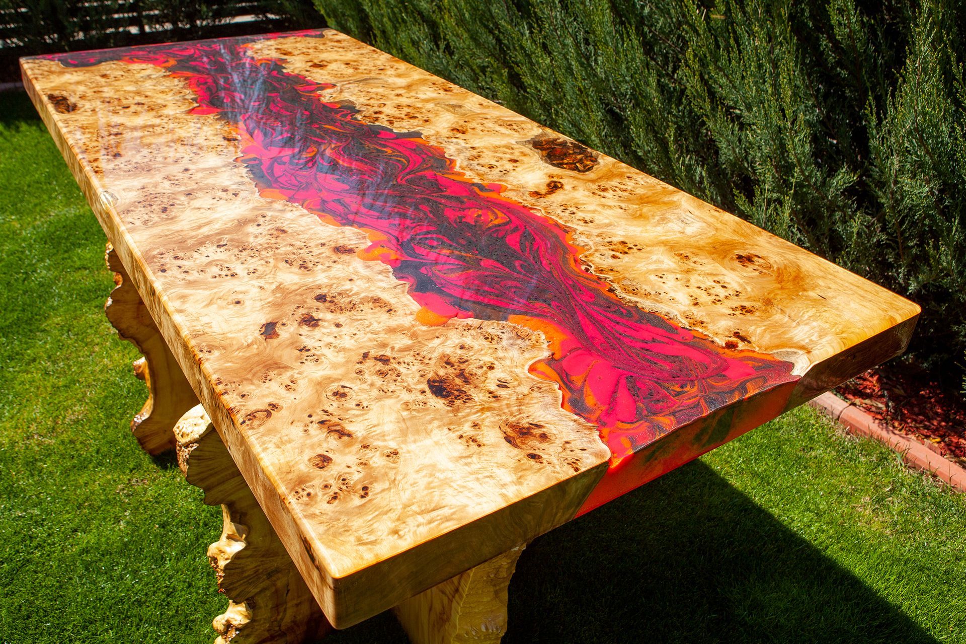 A rectangular table with a burl wood top featuring a vibrant, flowing river design of marbled red and orange resin.