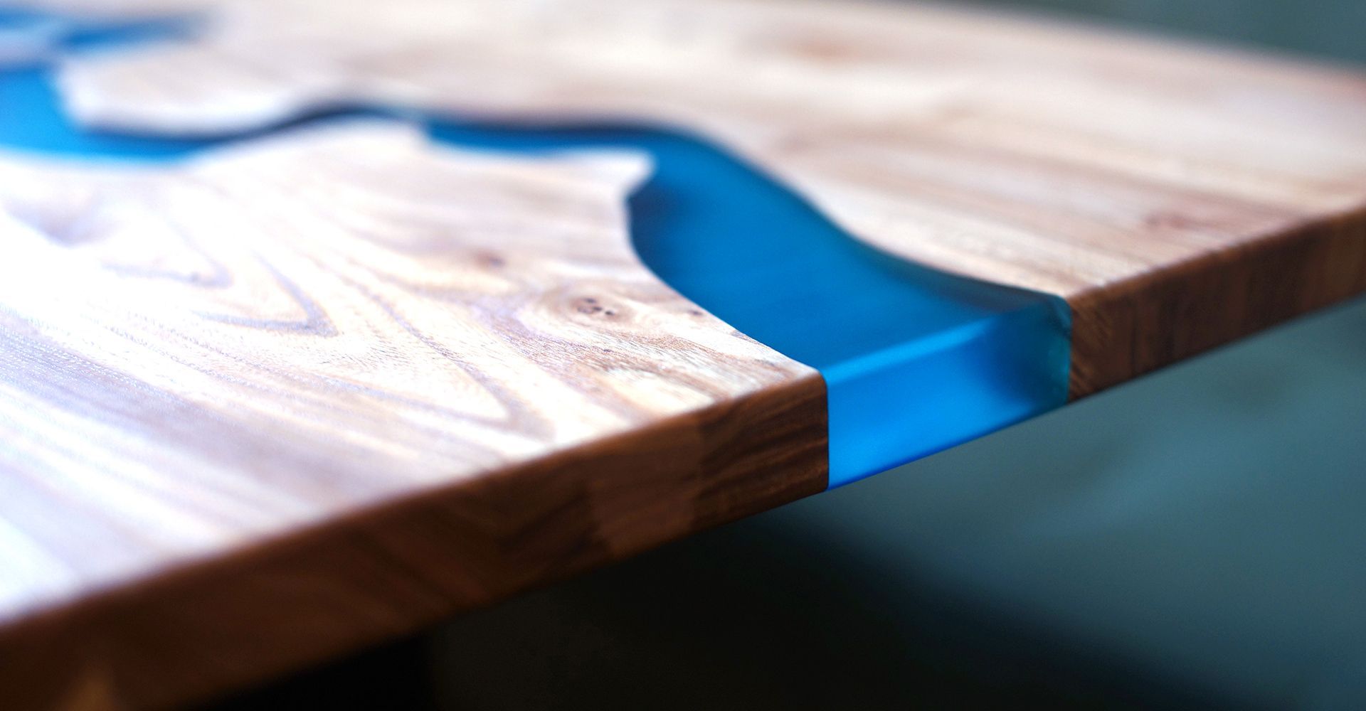 A wooden tabletop features a jagged center filled with translucent, vibrant blue epoxy resin.