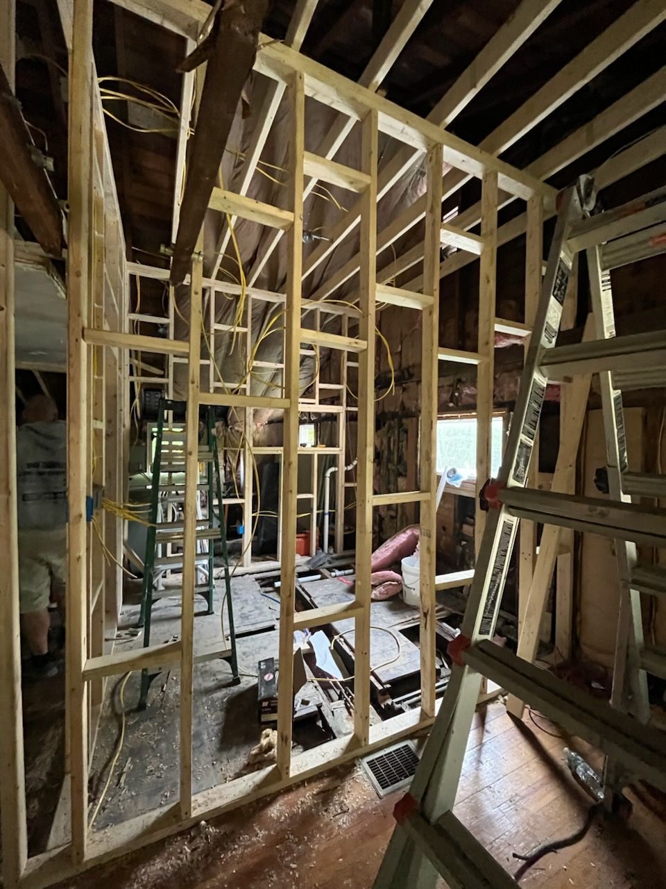 Wooden wall framing for a room renovation under construction, viewed from a doorway with a ladder in the foreground.
