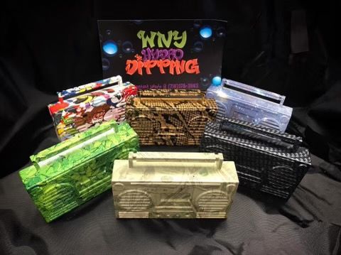 Six customized, patterned boombox models arranged in front of a WNY Hydro Dipping sign against a black background.