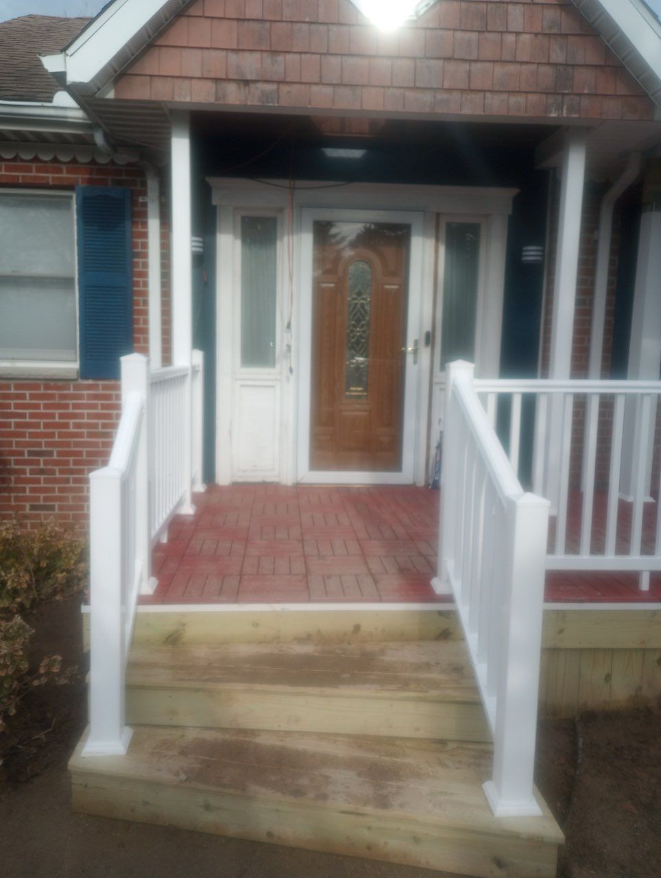 Wooden front steps leading to a porch with a red, stamped concrete landing and a wood-toned door with a glass inlay.