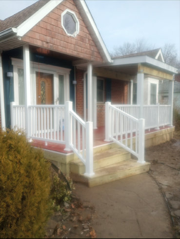 A house exterior with a wooden porch, white railings, and steps leading to a wood-paneled entrance with a small window.