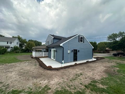 A blue-sided house with a newly poured concrete patio and an adjacent white-fenced porch under a cloudy sky.