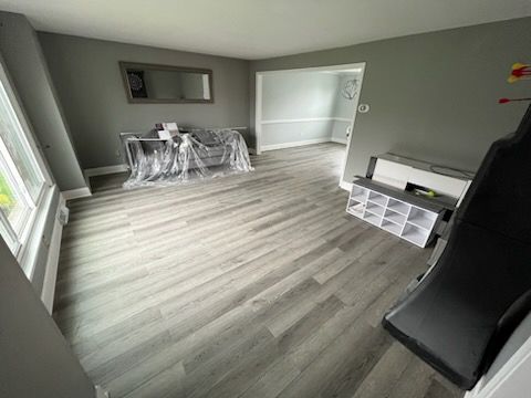 A spacious room with grey walls and light wood-patterned flooring, featuring a plastic-covered sofa and storage unit.