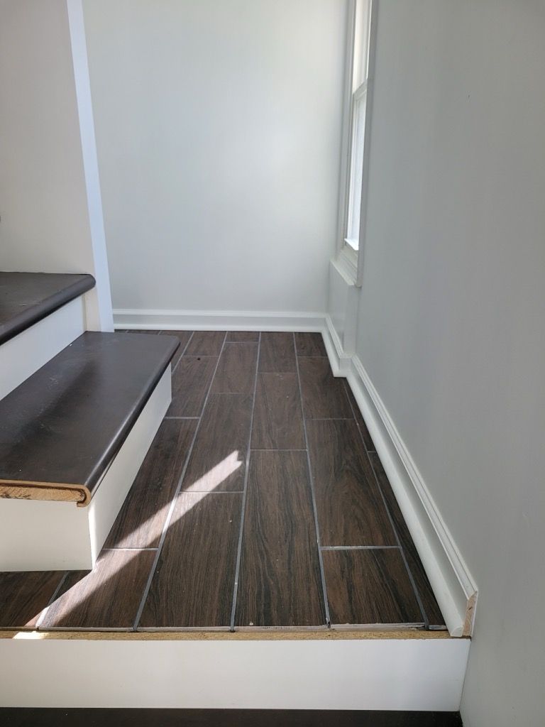 A landing with dark wood-look tile flooring next to a staircase with dark treads and white risers, framed by baseboards.