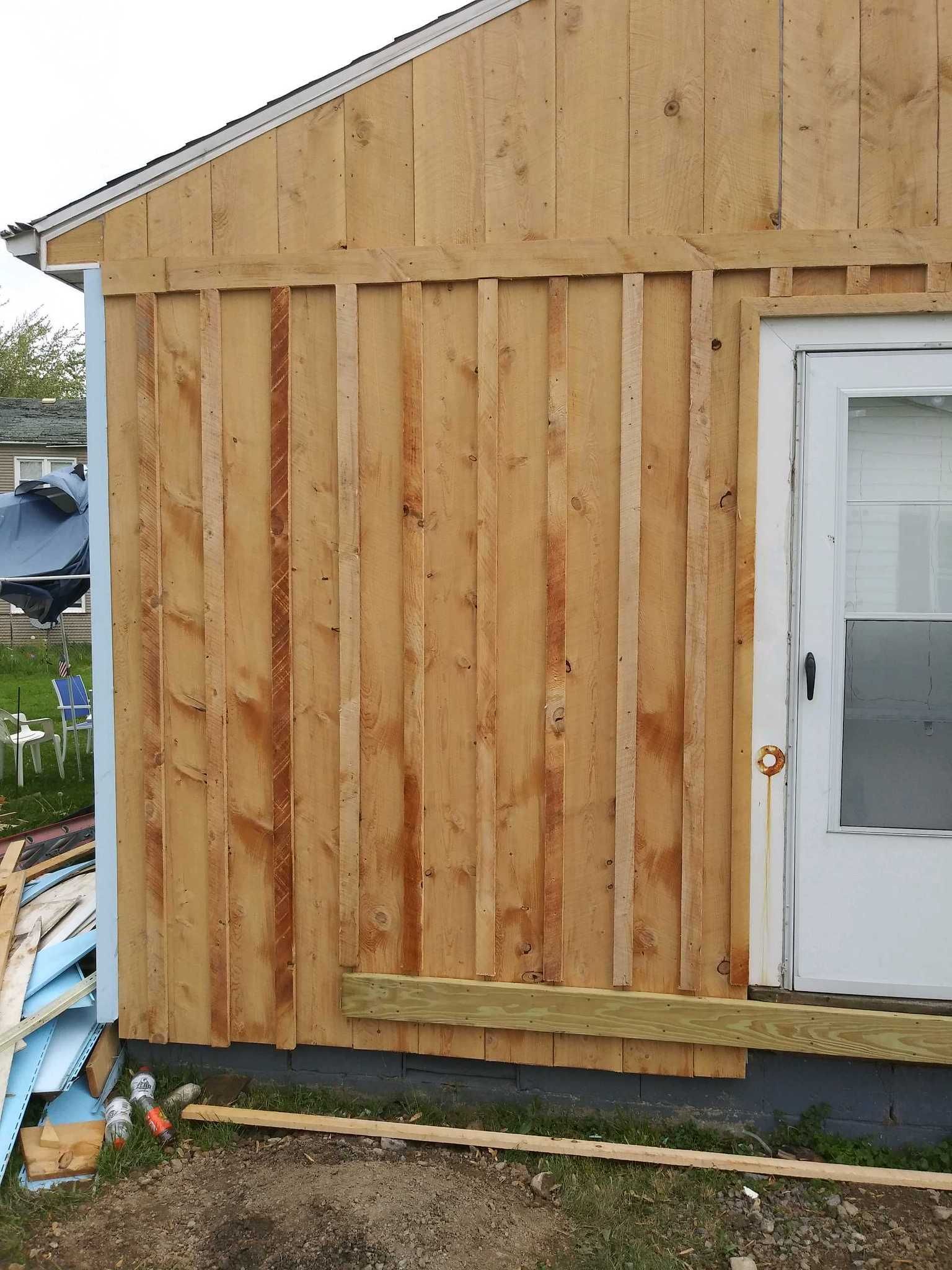 An exterior wall with vertical wood siding and a white door, currently under construction with exposed wooden trim.