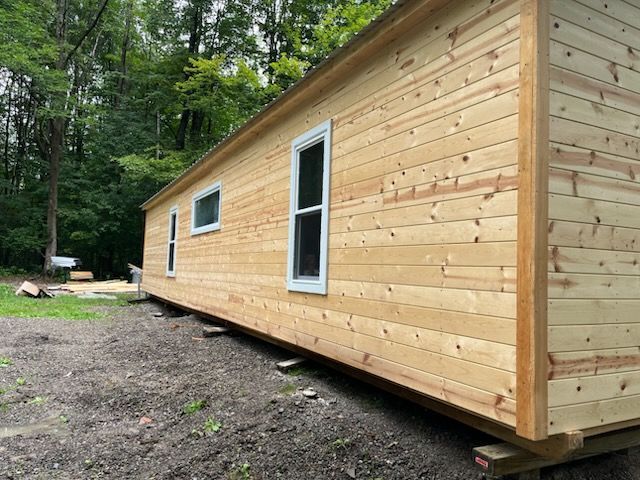 An unfinished wooden cabin with white-trimmed windows sitting on temporary supports in a wooded area.