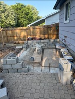 Construction of a concrete block outdoor structure or patio in a backyard with a wooden fence and a house wall.