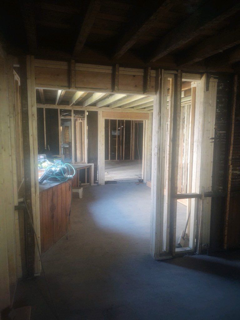 Interior view of a residential construction site showing wooden wall framing and open doorways under exposed ceiling joists.