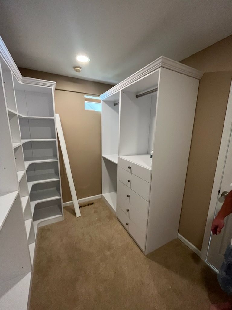 A partially installed white closet organizer system in a walk-in closet with tan carpet and brown walls.