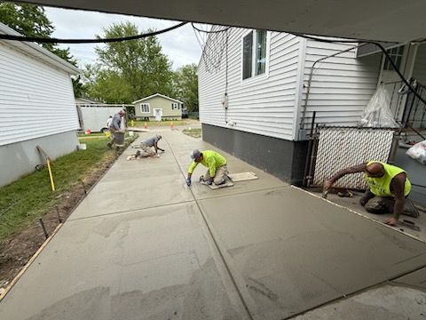 Workers in high-visibility vests finish smoothing a newly poured concrete driveway between two residential homes.