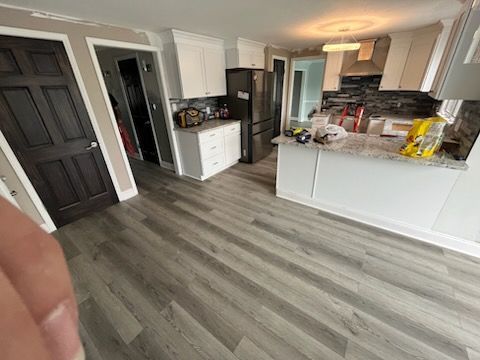 Modern kitchen interior with white cabinets, gray wood-look flooring, granite countertops, and stainless steel appliances.