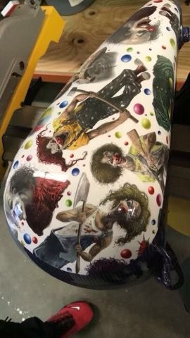 A white motorcycle tank decorated with a repeating pattern of colorful, menacing zombie illustrations and small spheres.