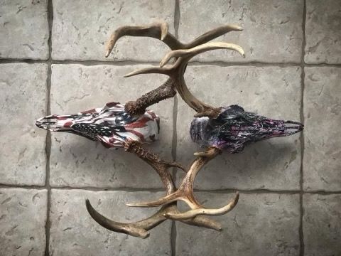 Two deer skulls with antlers, one painted with an American flag pattern and one with dark camouflage, placed on tile.