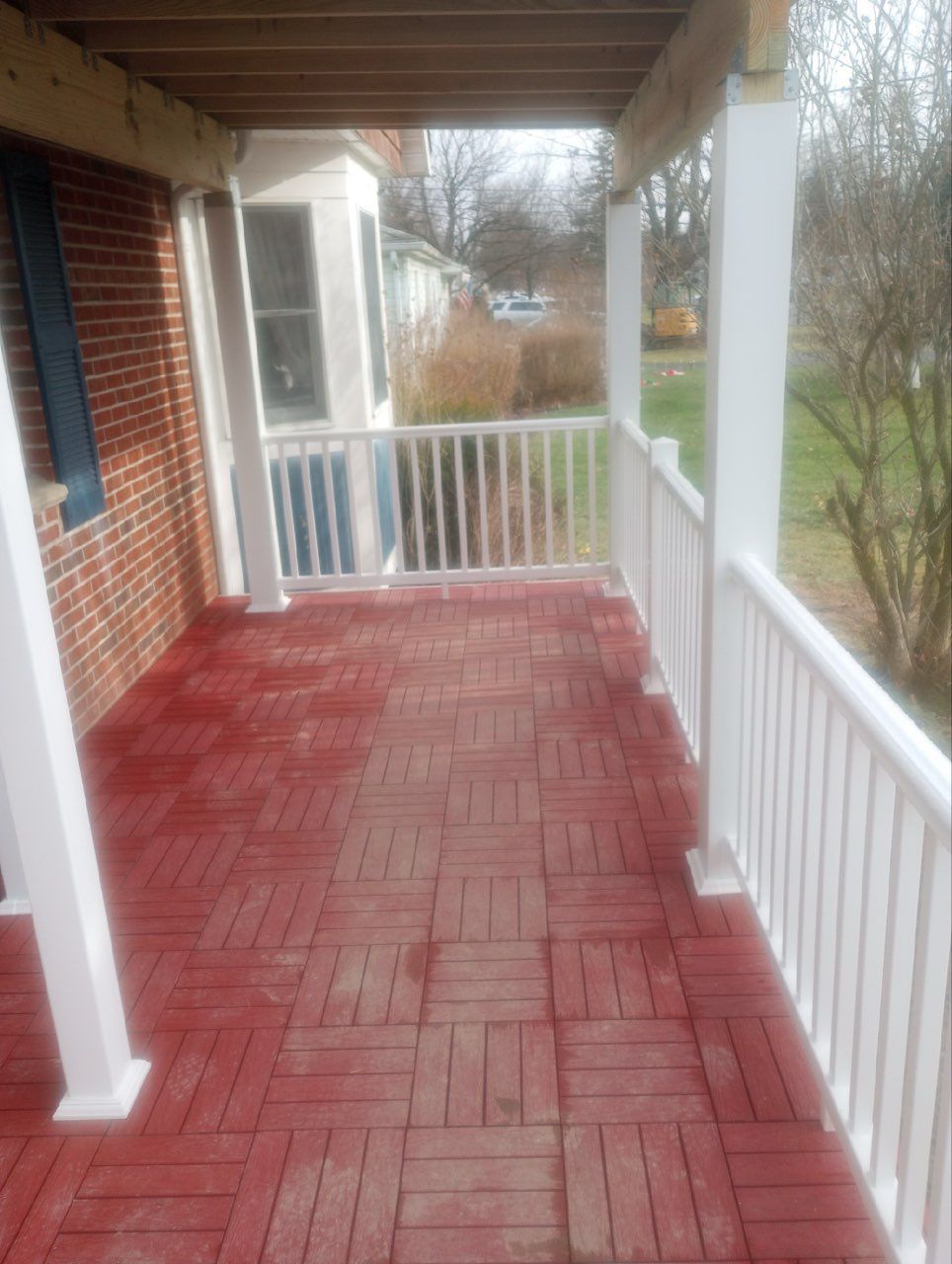 A red tiled porch with white railings and support posts, situated next to a red brick house wall.