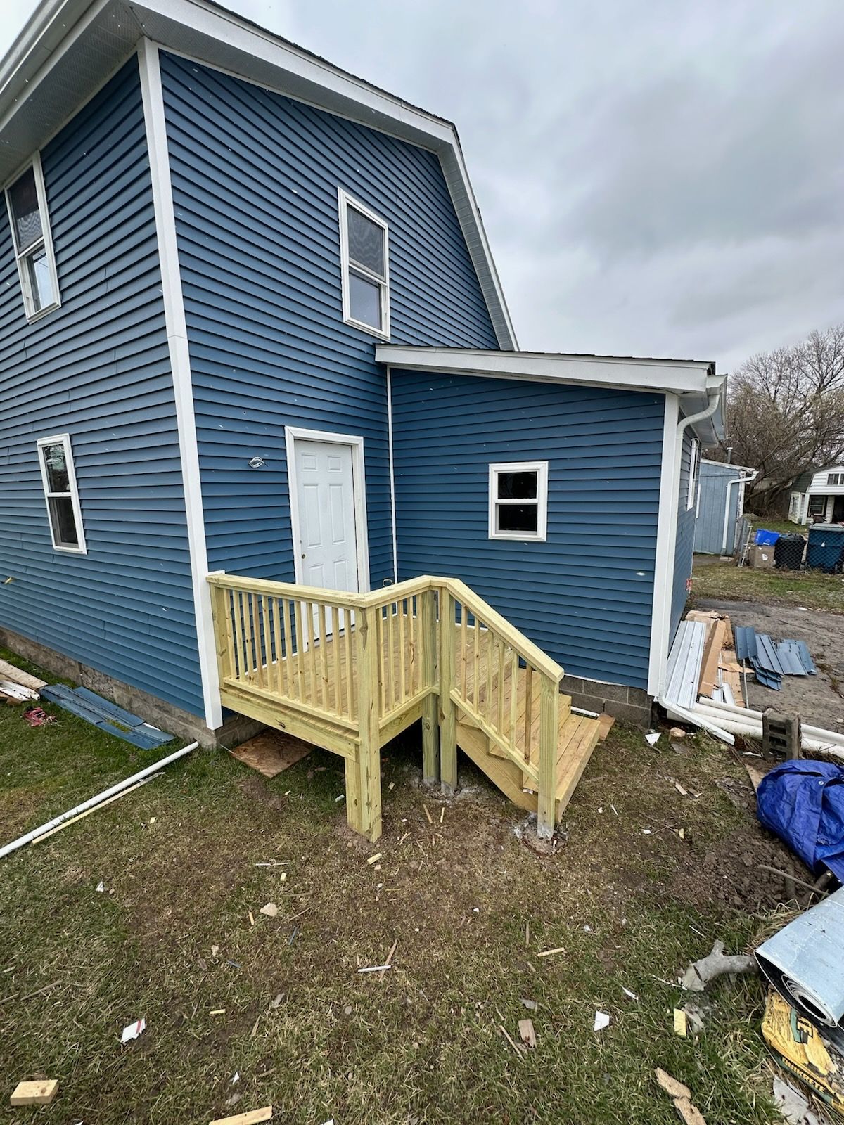 A blue-sided house with a newly constructed wooden deck and staircase leading to a side entrance door.