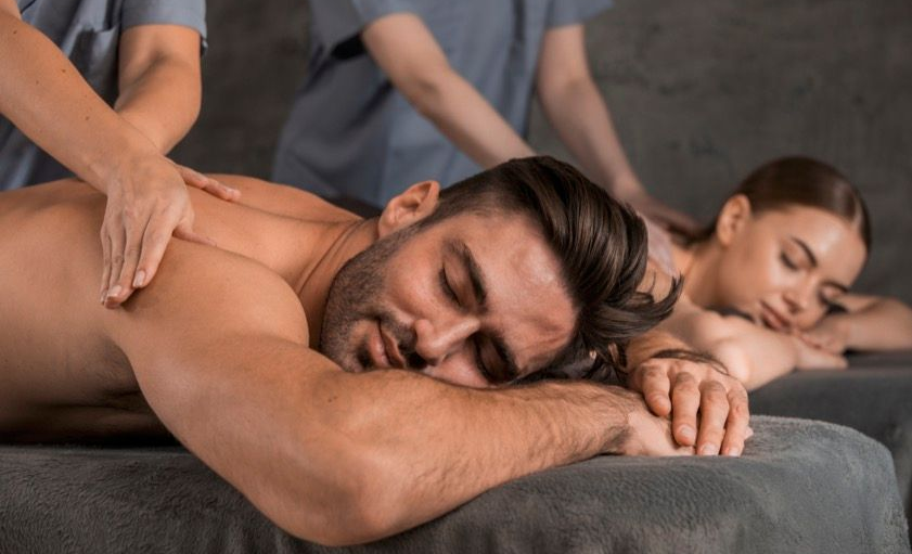 Personen, die in einem Spa auf dunklen Massageliegen massiert werden
