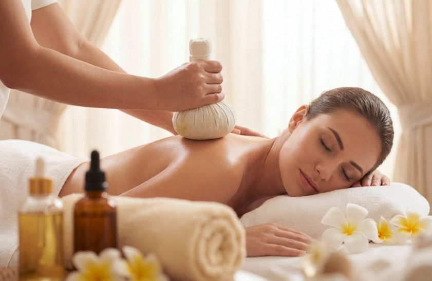 Eine Spa-Therapeutin massiert einer Frau, die entspannt auf einer Liege liegt, mit einer Bürste den Rücken