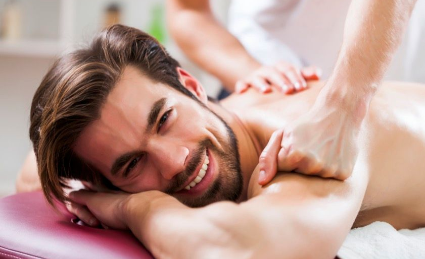 Lächelnder Mann, der auf einer Liege eine Schultermassage bekommt