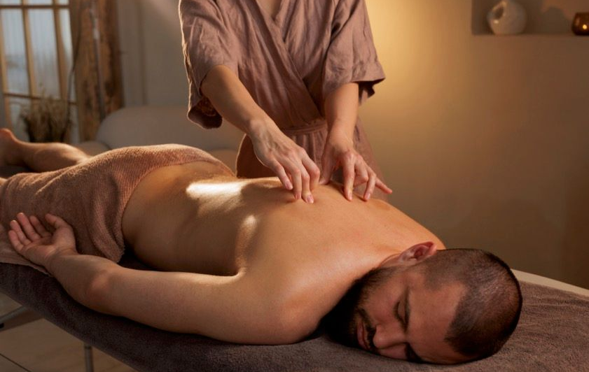 Ein Masseur massiert den Rücken eines Mannes, der bäuchlings auf einer Liege liegt