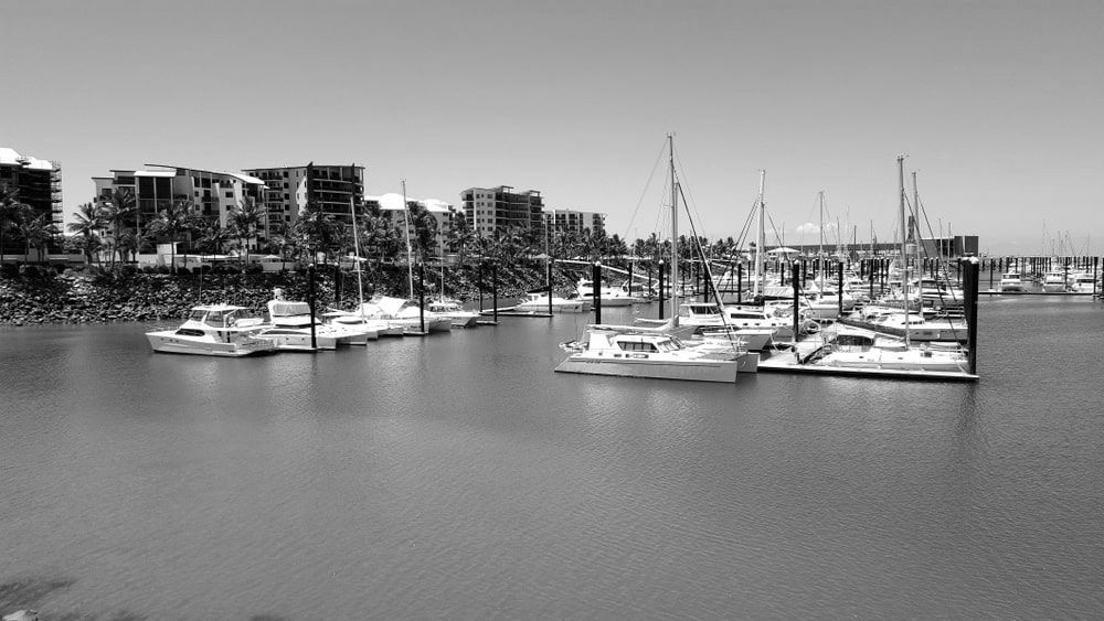 A Row Of Boats Are Docked In A Marina With Buildings In The Background — Lux Noir In Mackey, QLD