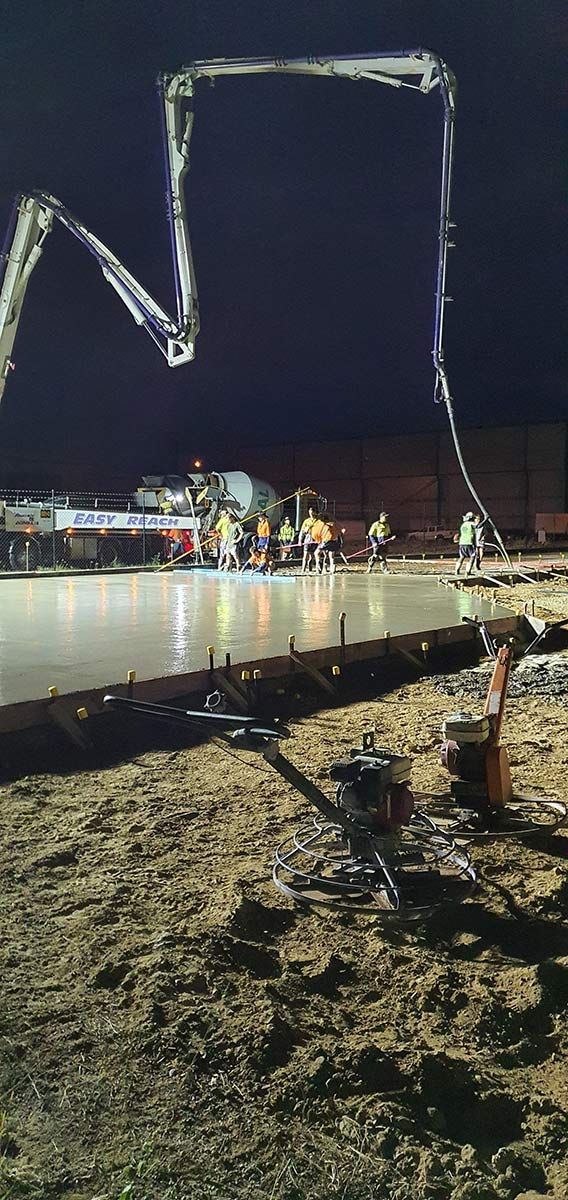 A concrete pump is pouring concrete on a construction site at night.