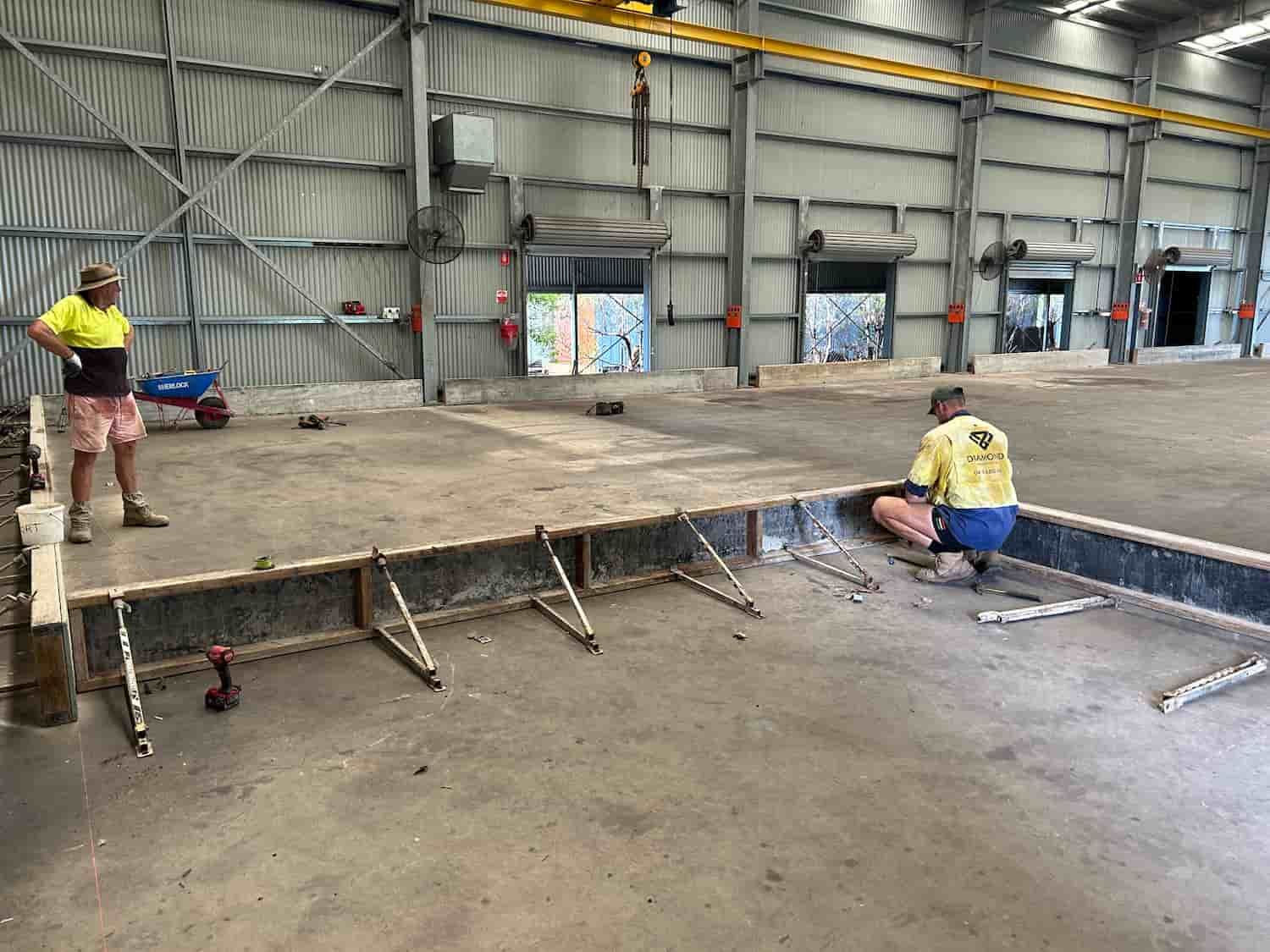 Two Men Are Working on a Concrete Floor in a Warehouse — Diamond Concreting In Mount Low, QLD