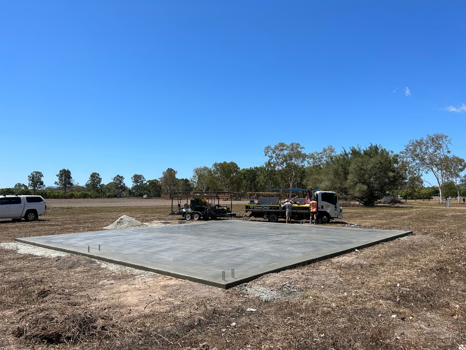 Wheelbarrow In The Grass Next To A Trowel On A Concrete Surface — Diamond Concreting In Mount Low, QLD