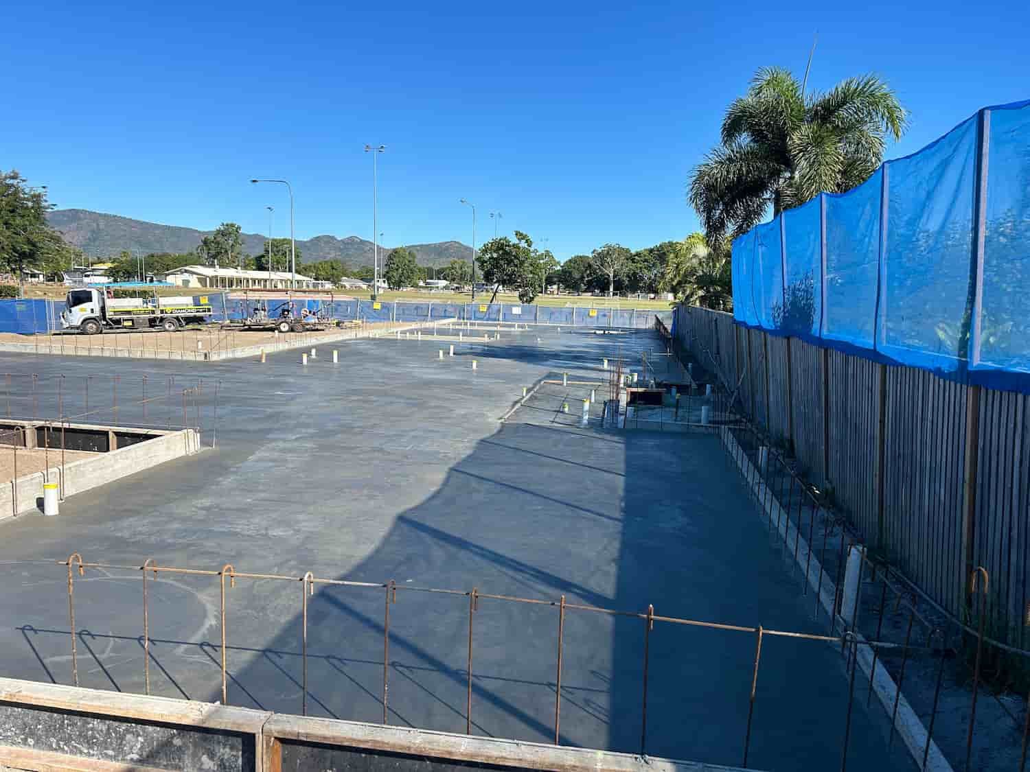 A Construction Site With a Blue Fence and a Truck in the Background — Diamond Concreting In Mount Low, QLD
