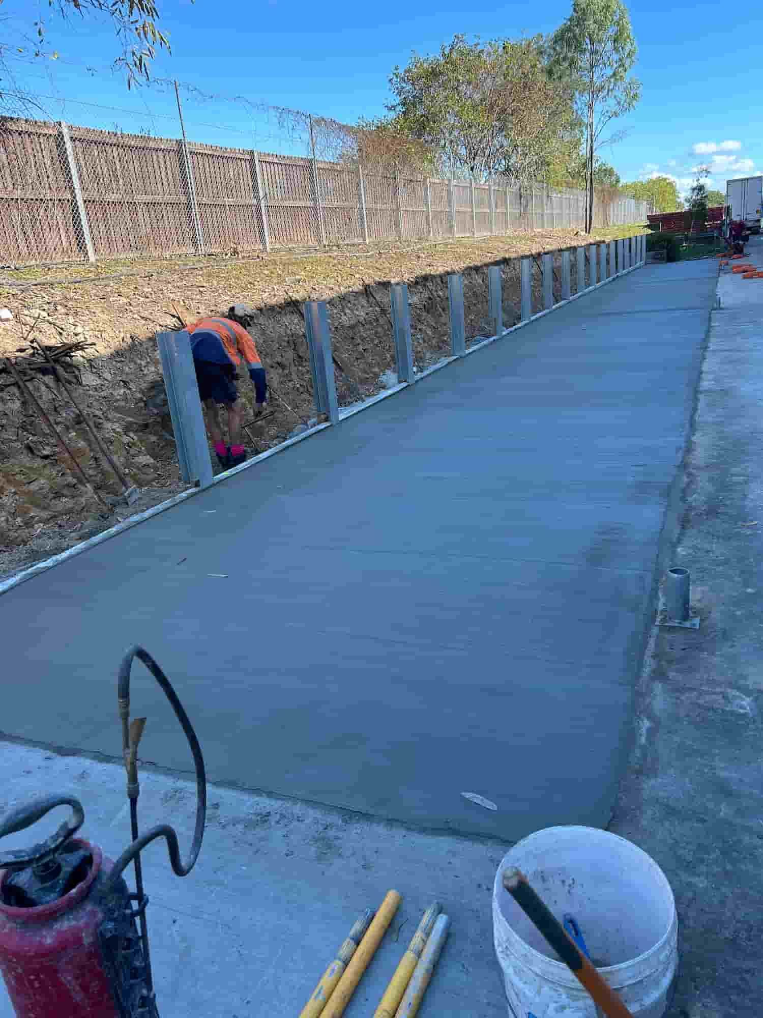 A Man is Working on a Concrete Driveway Next to a Fence — Diamond Concreting In Mount Low, QLD