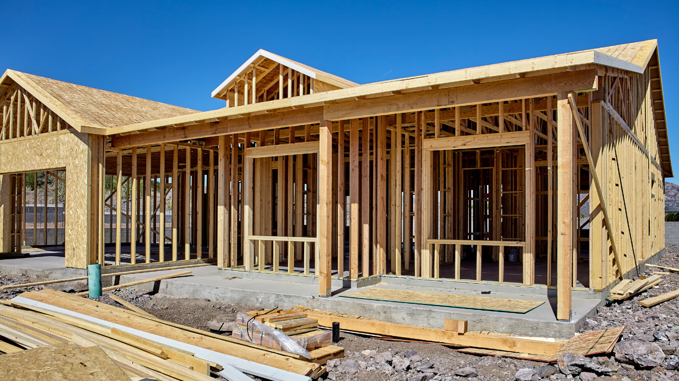 House under construction with wooden frame against a blue sky.