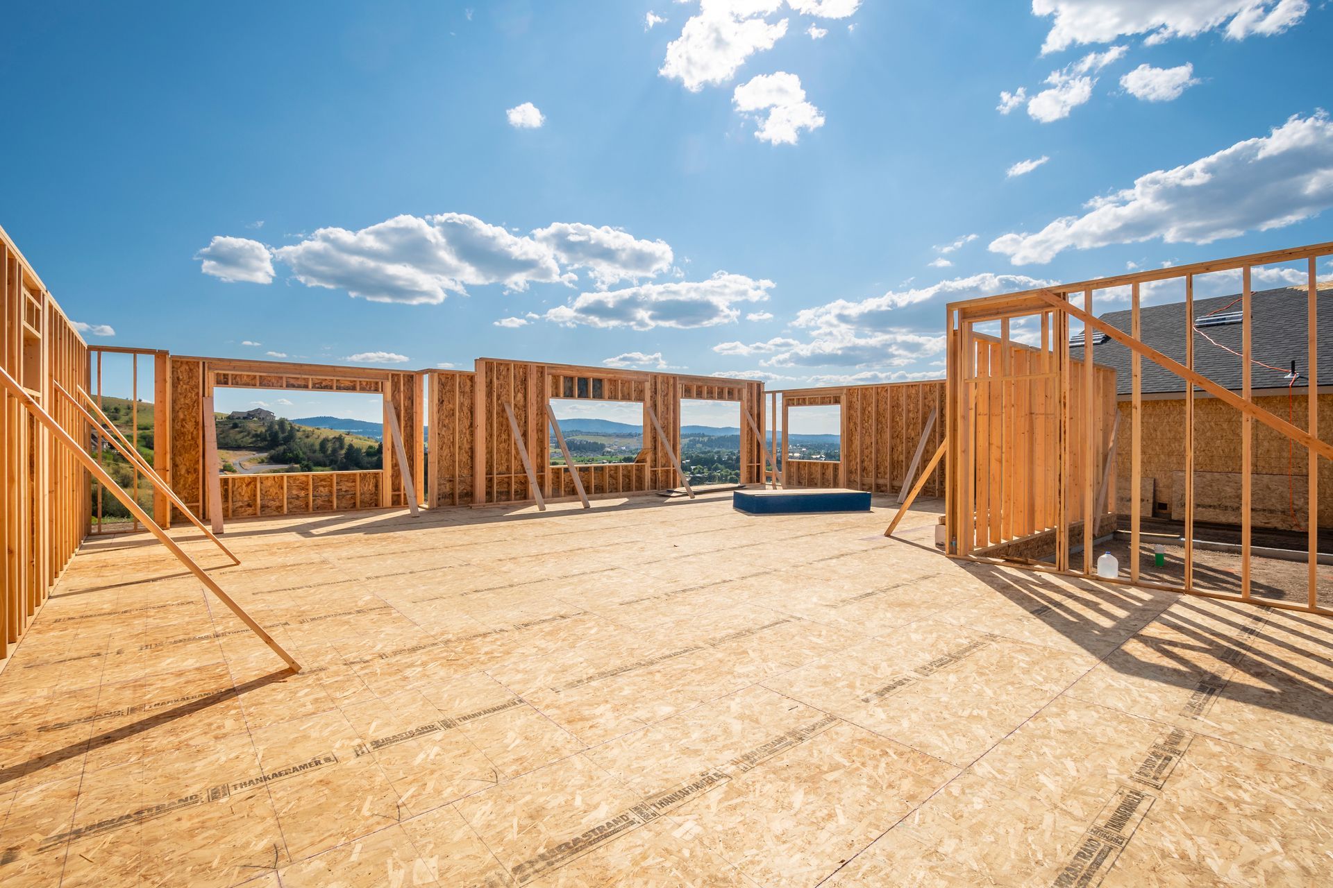 Wood frame of a house under construction; open to the sky and a distant landscape on a sunny day.