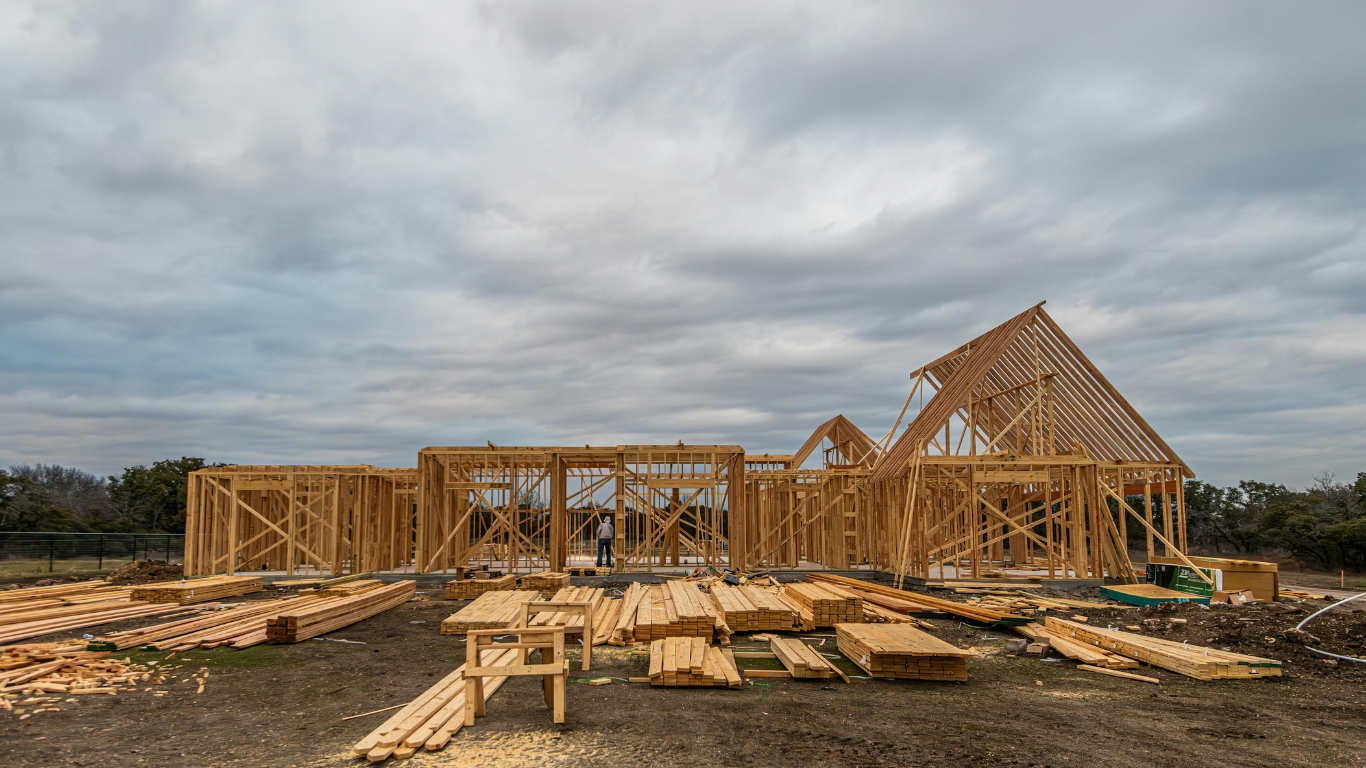 Wooden frame of a house under construction on a cloudy day. Lumber is scattered on the ground.