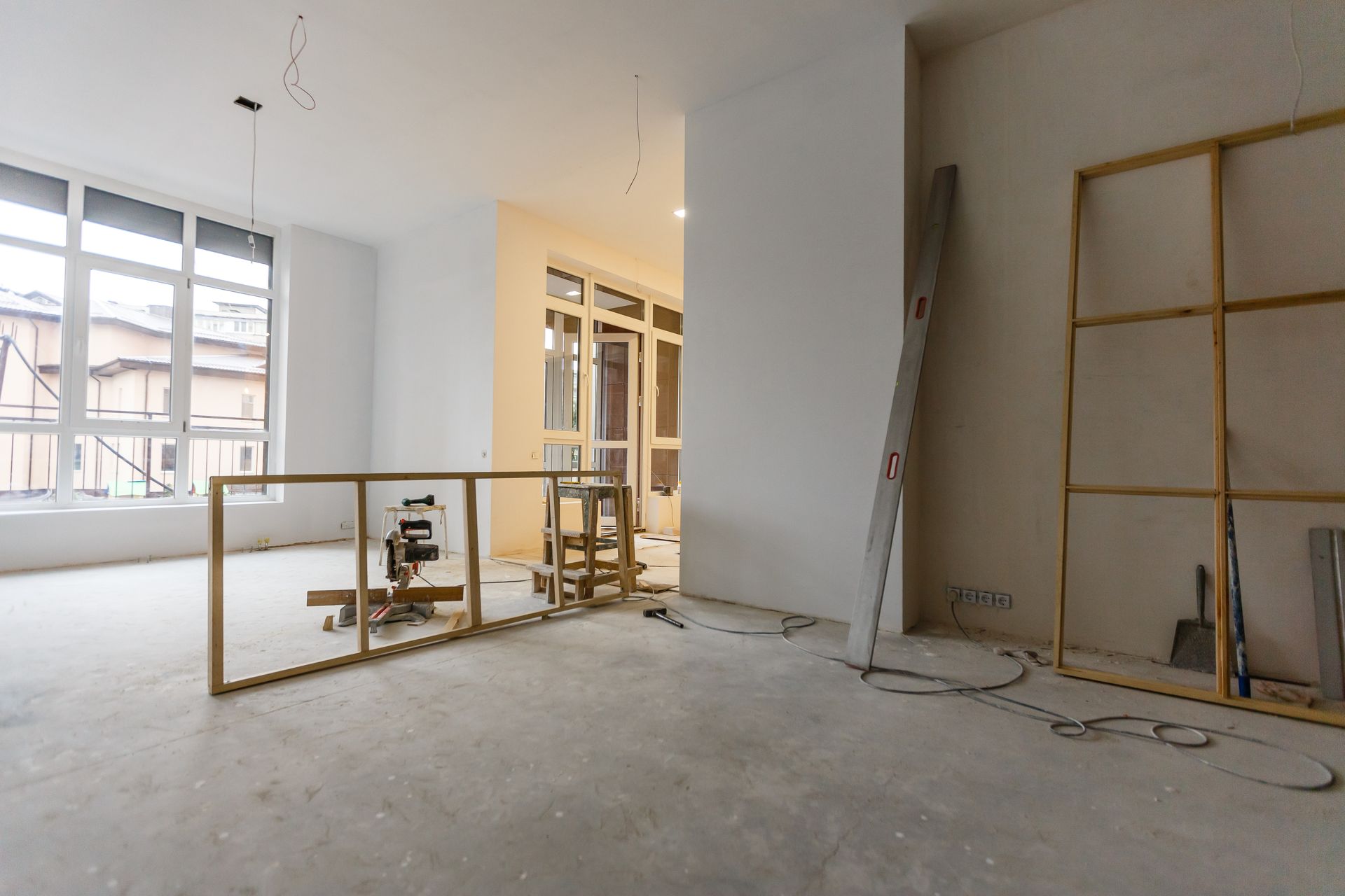 Interior renovation, empty room with concrete floor, windows, wooden frames, and construction materials.