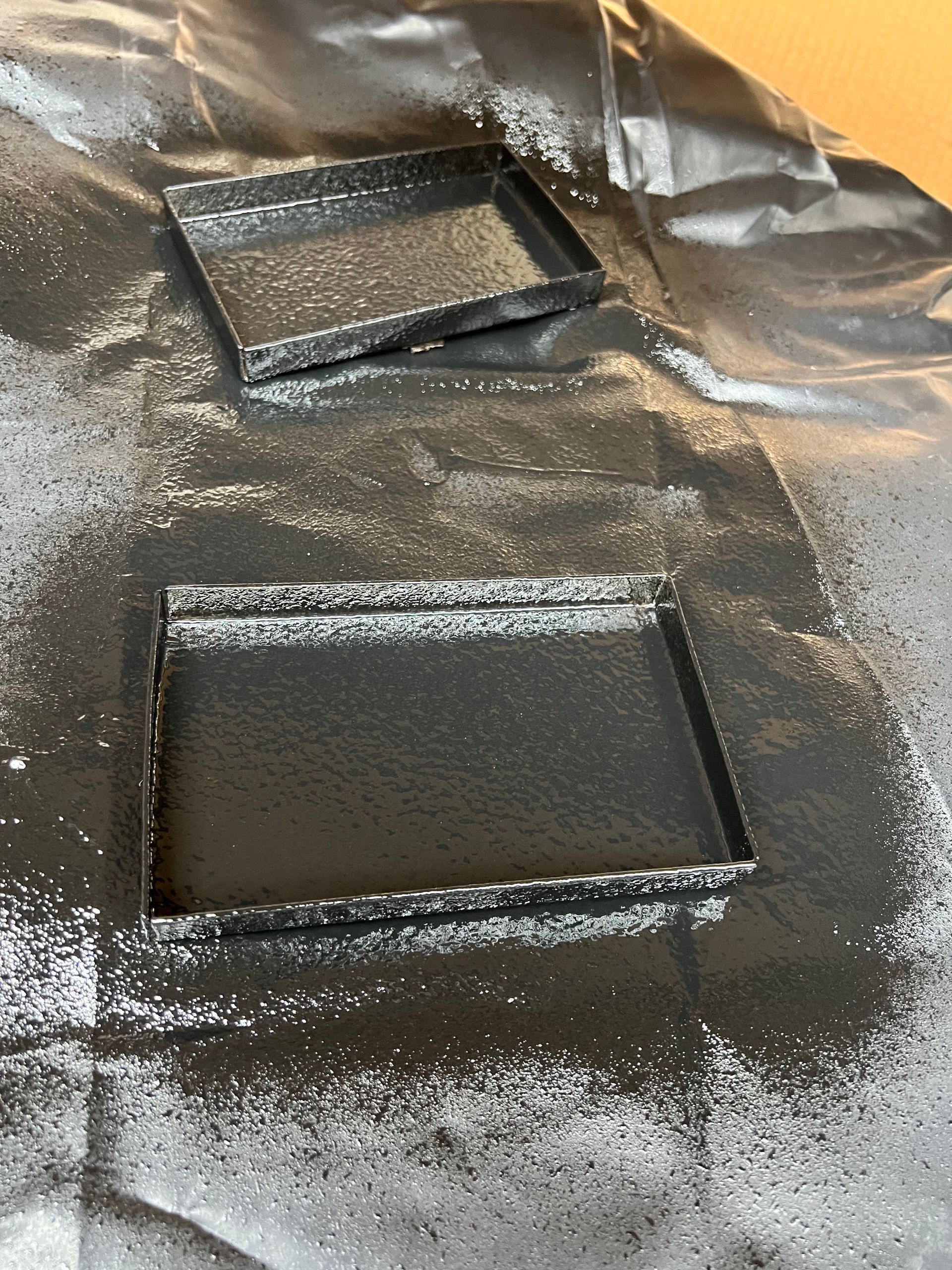 Two square trays are sitting on a piece of aluminum foil covered in black paint.