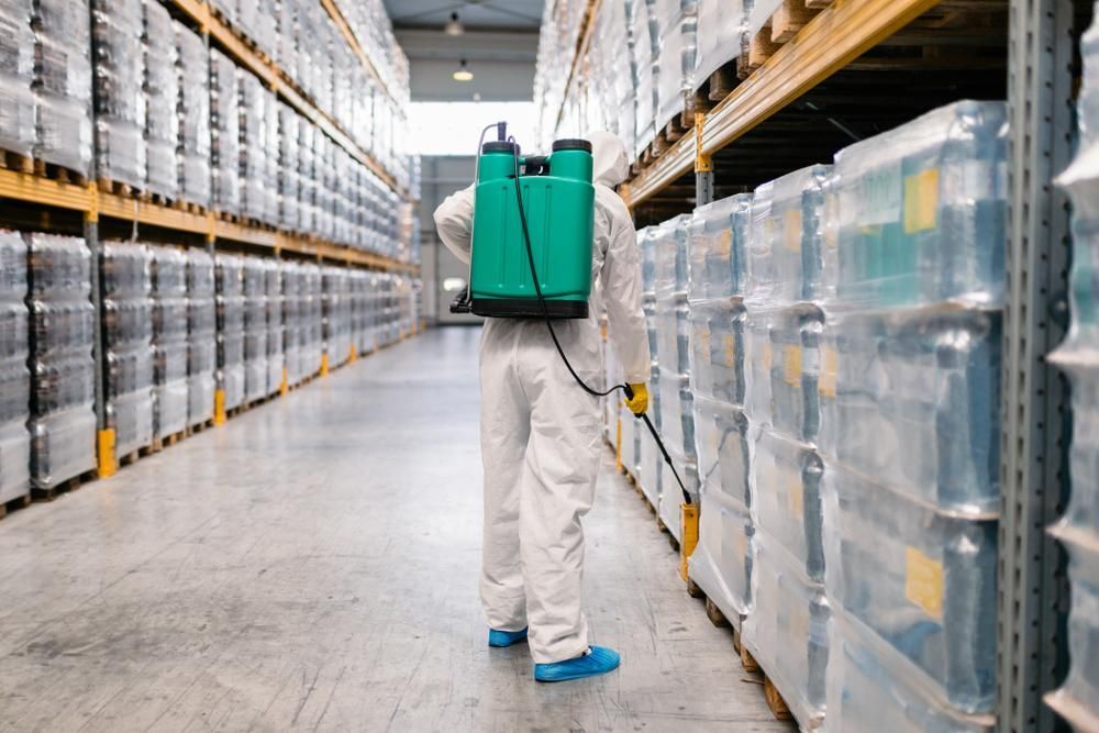 A Man in A Protective Suit Is Spraying a Warehouse with A Sprayer — PDM Pest Control in Craiglie, QLD