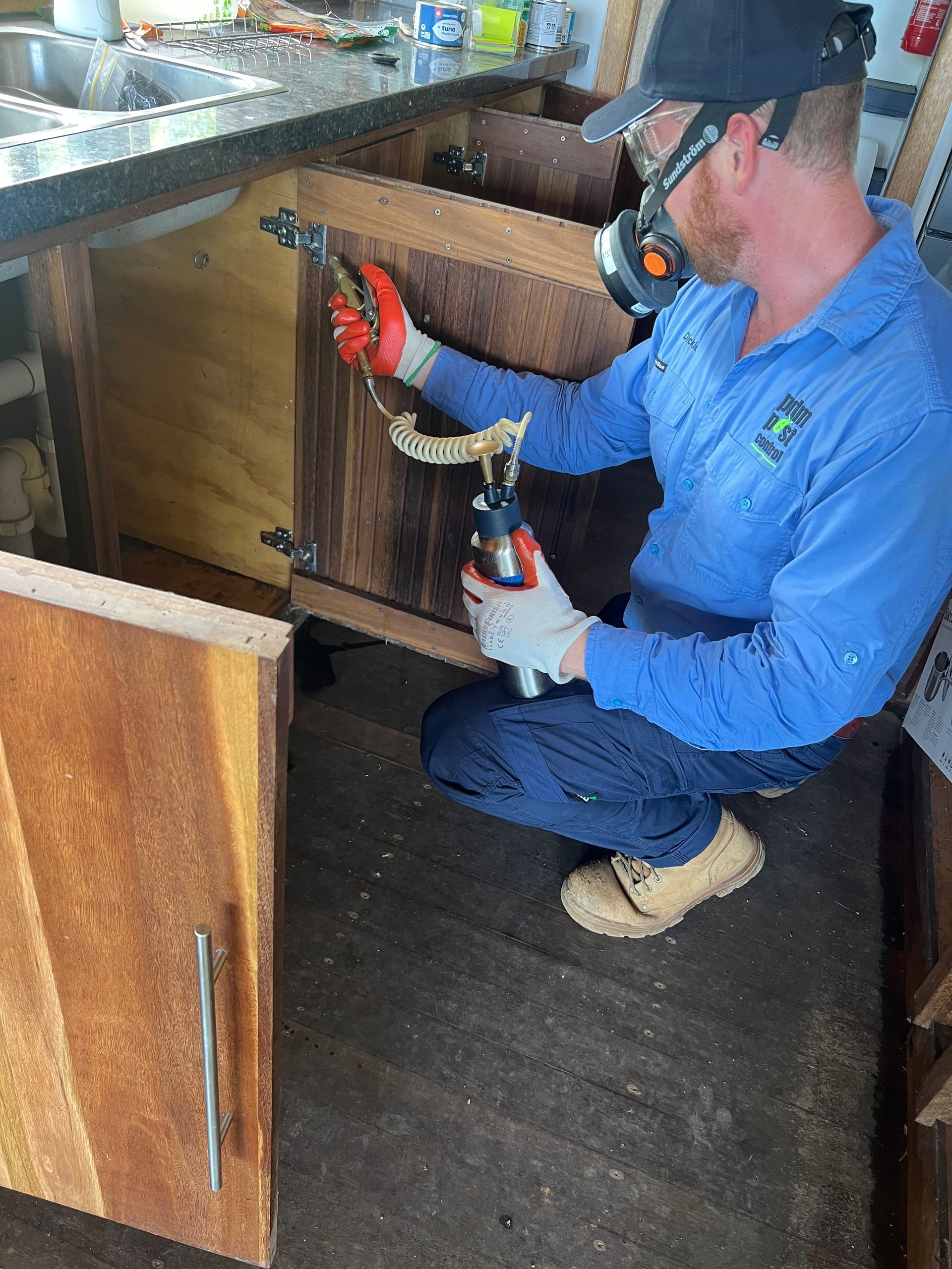 A Man in A White Suit Is Kneeling Down in A Corner of A Room — PDM Pest Control in Trinity Beach, QLD