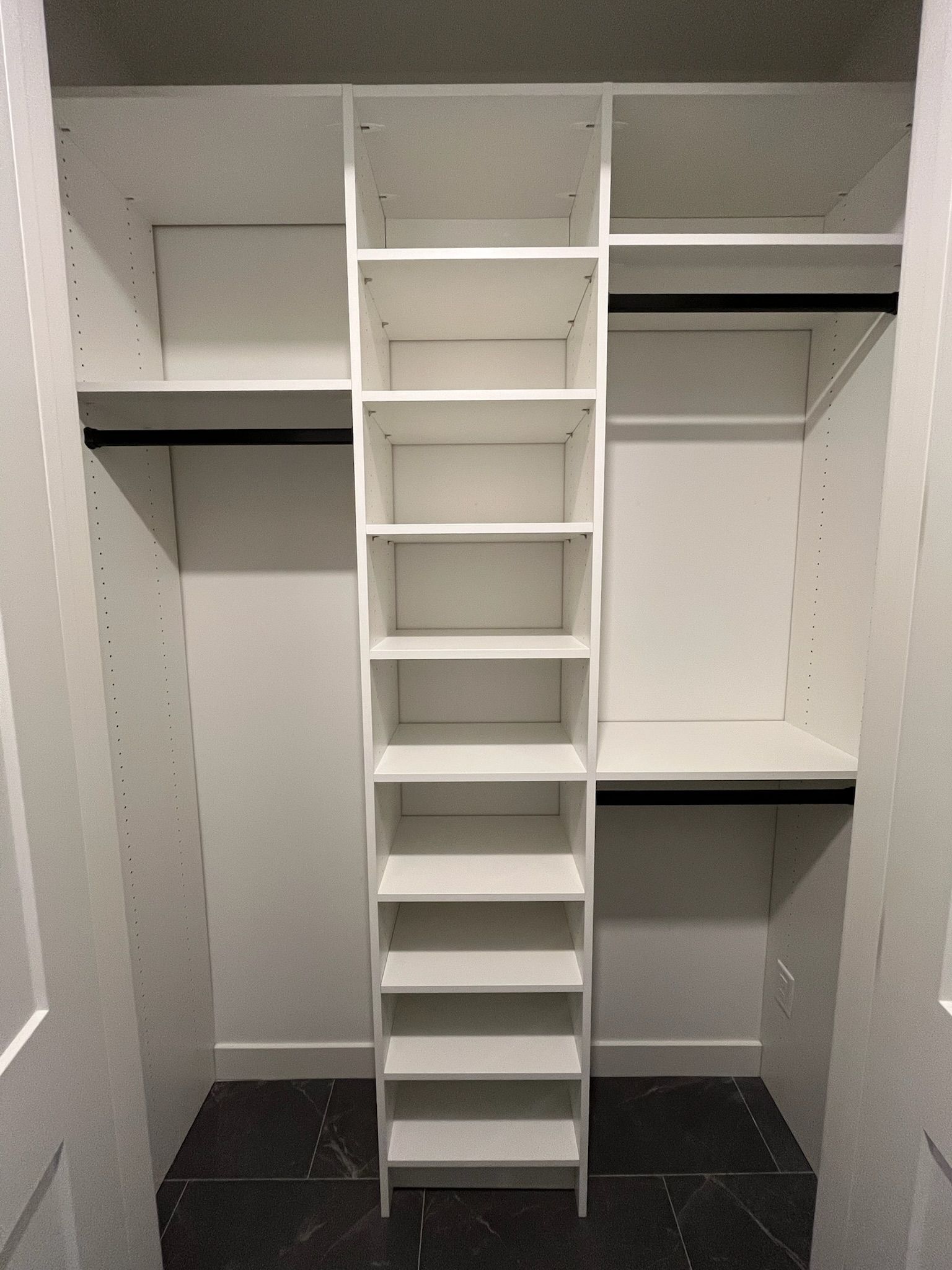 Walk-in closet with white shelves, hanging rods, and a central ladder against dark tile floor.