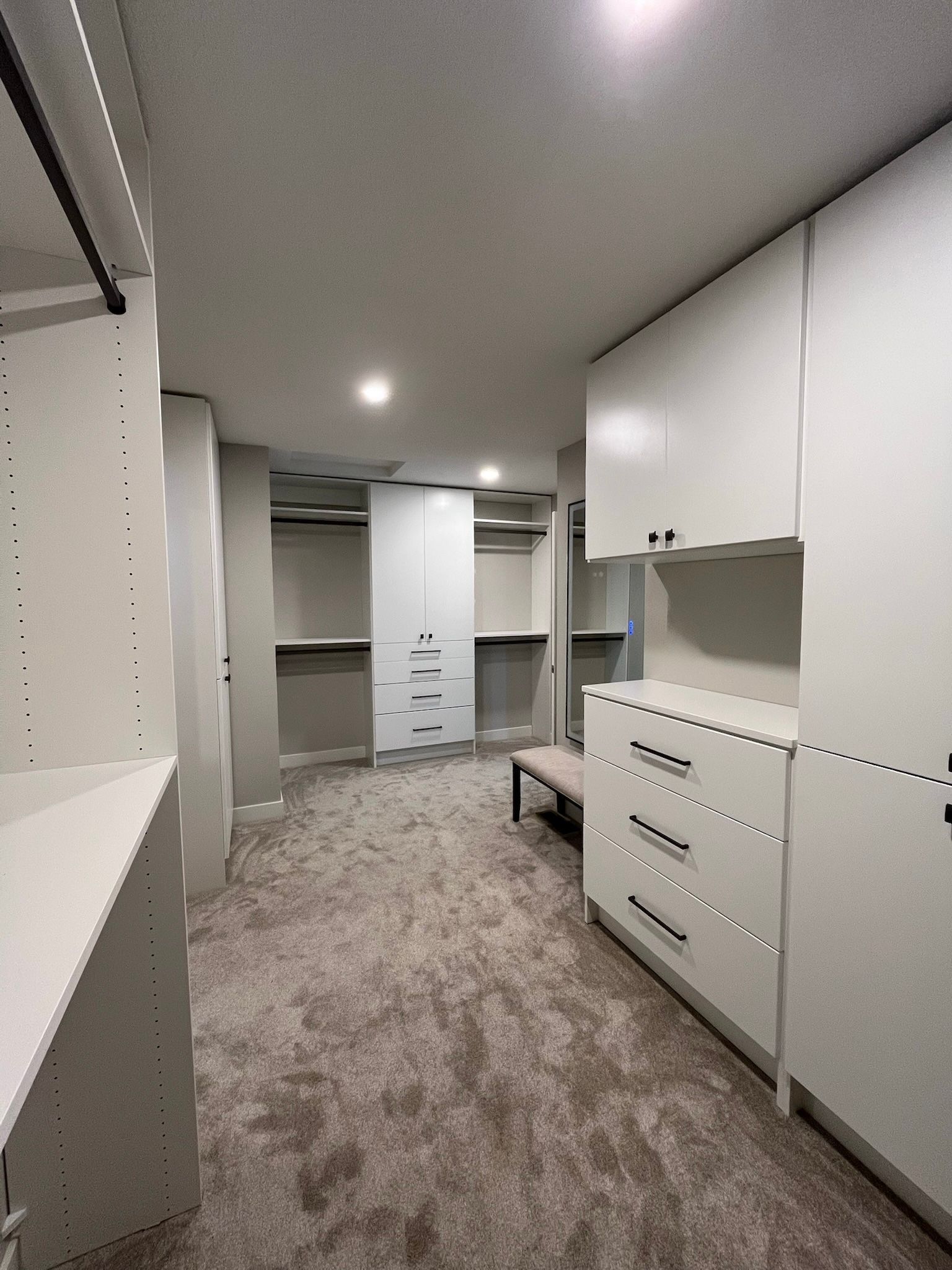 Modern walk-in closet with white cabinets, drawers, shelves, and gray carpeted floor