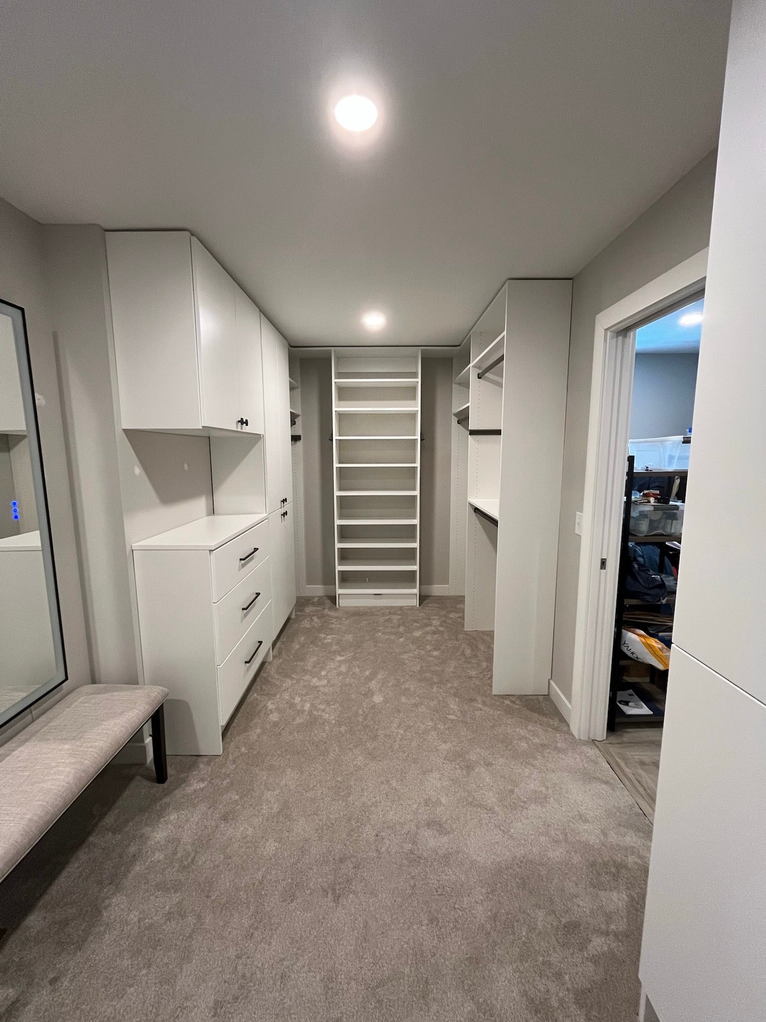 Bright walk-in closet with carpet, white shelves, and central staircase-like shelving.