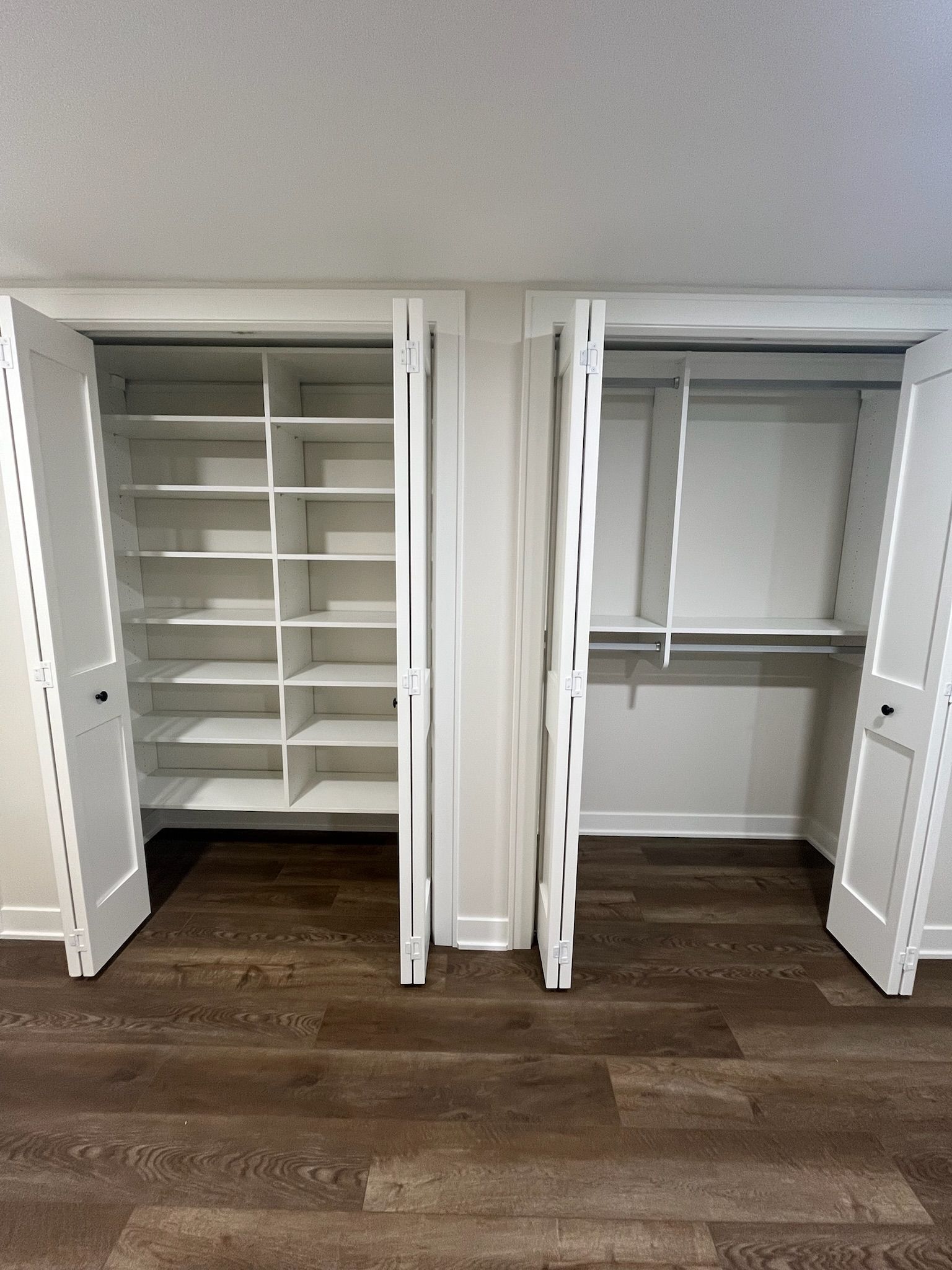 Open white closet with shelves and hanging rods on a wood floor