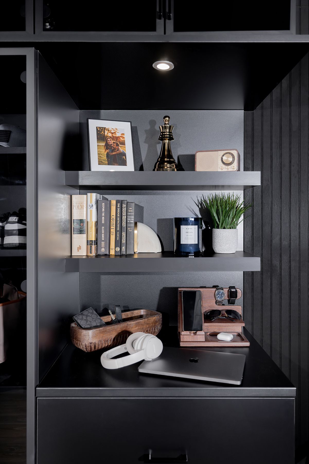 Black shelving nook with books, framed art, decor, a plant, and shoes above a desk drawer