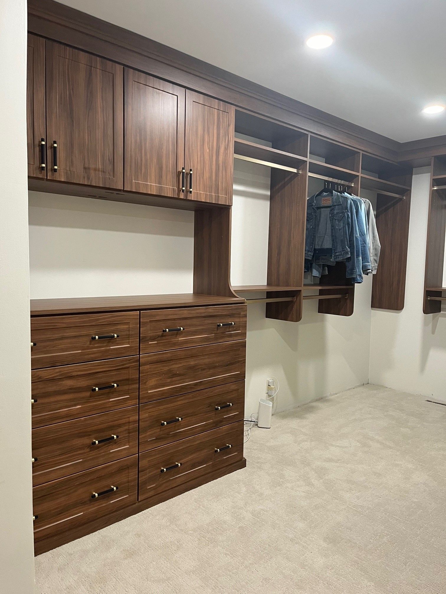 Built-in walk-in closet with wood drawers, shelves, and hanging clothes on the right.