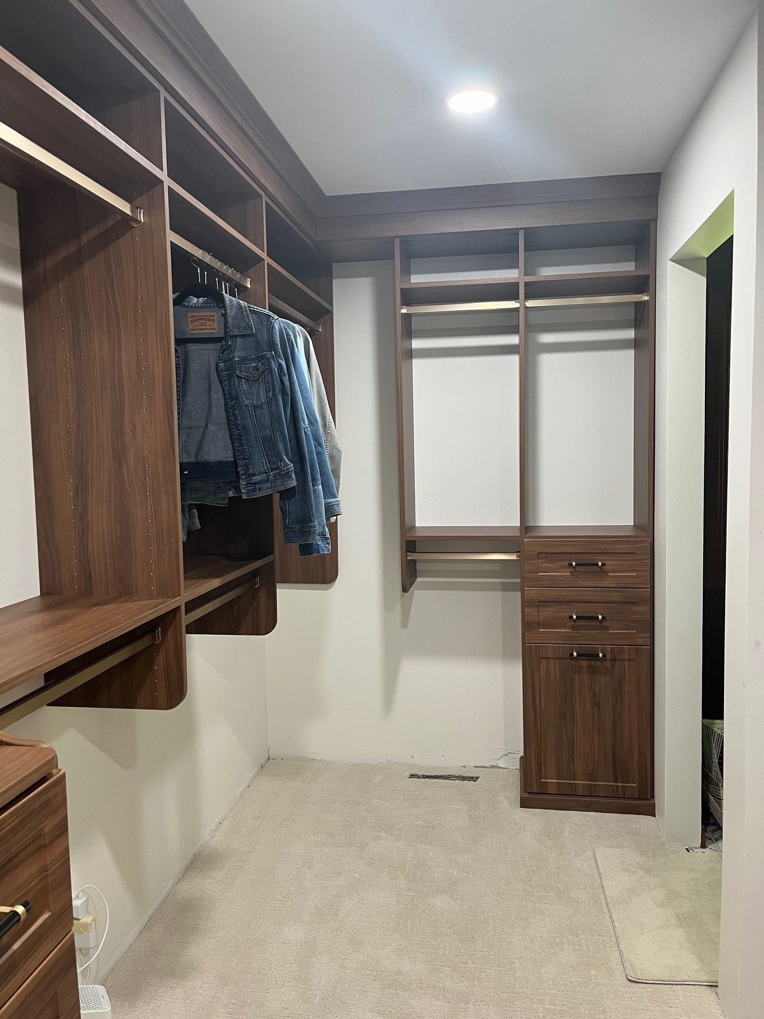 Walk-in closet with wooden shelving, hanging clothes, drawers, and a white tiled floor.