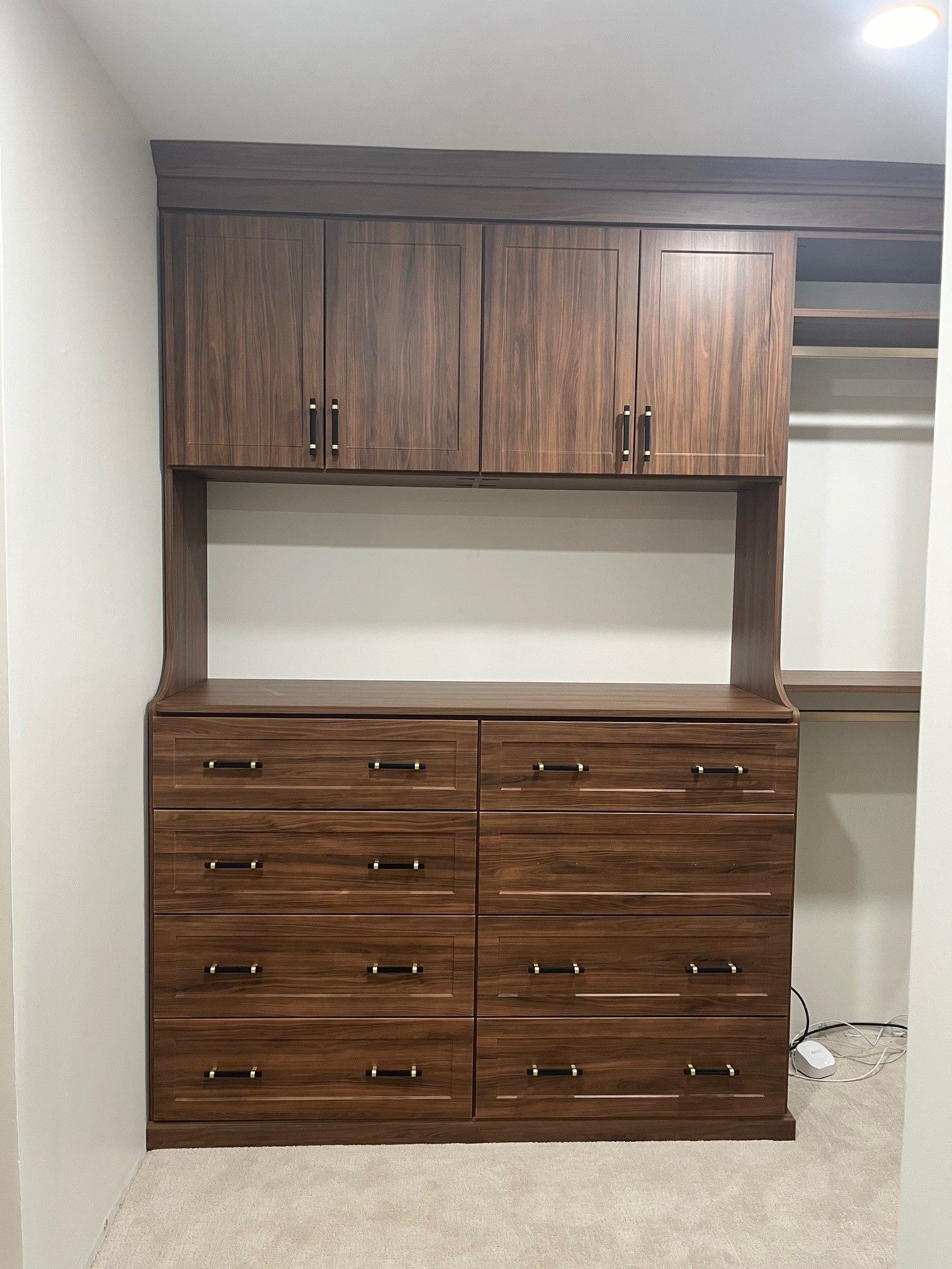 Built-in dark wood desk and cabinet storage unit in a room with white walls and carpet.