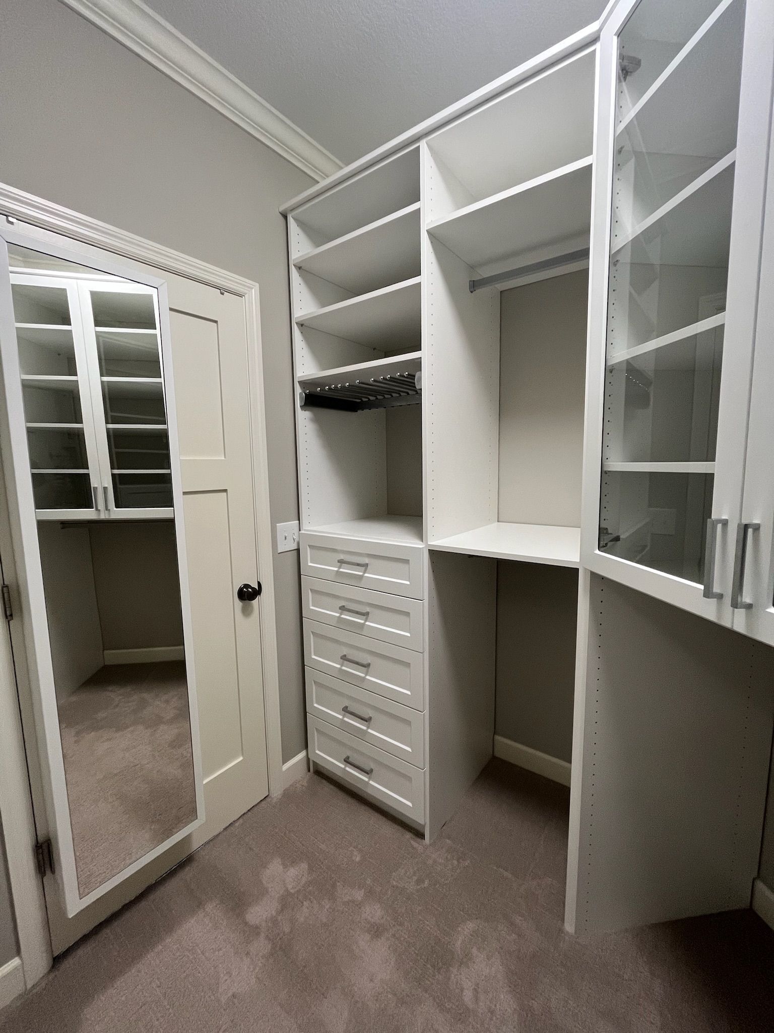 Walk-in closet with white shelving, drawers, hanging space, and mirrored door; carpeted floor.
