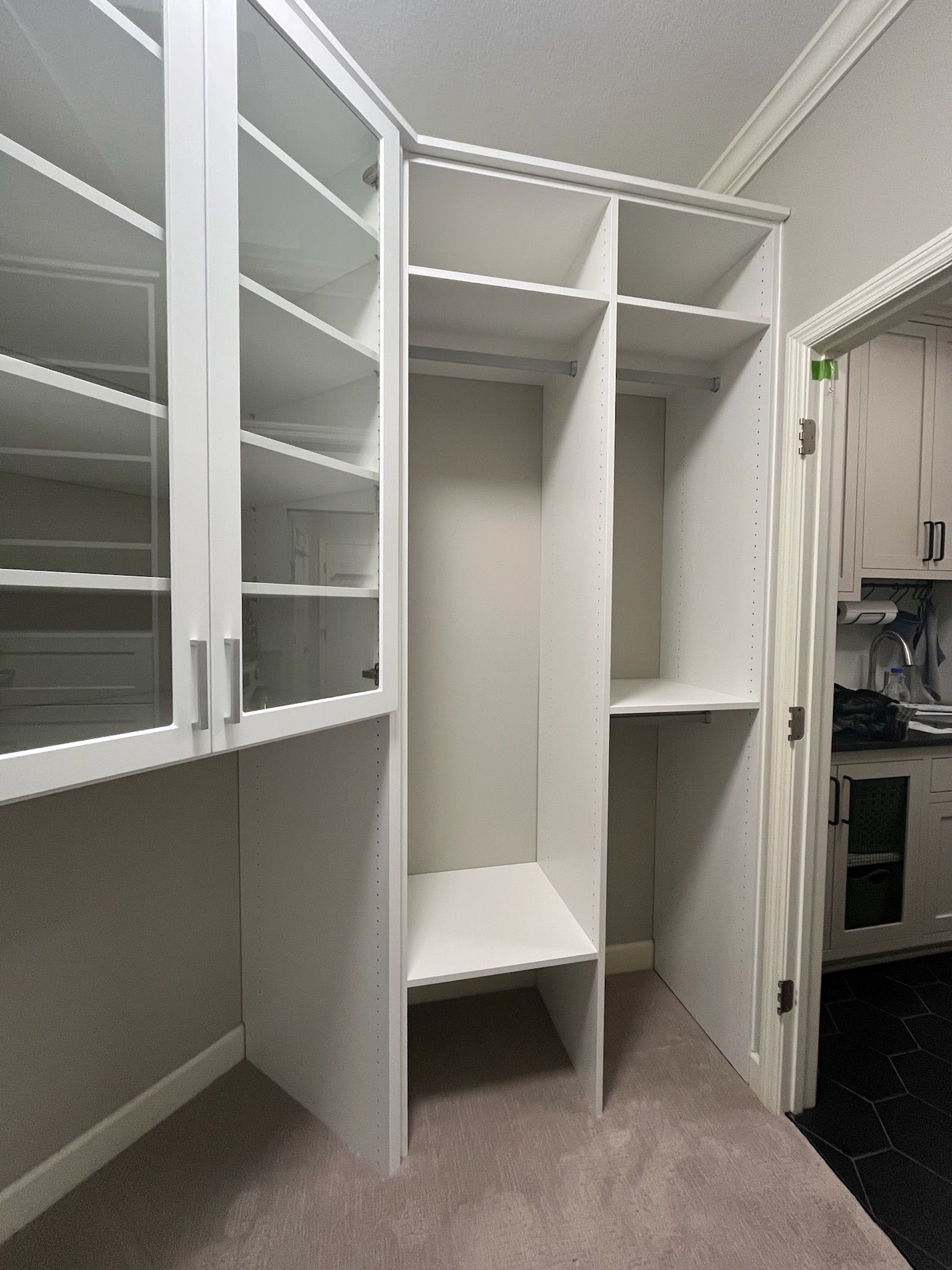 Empty white closet with built-in shelves, hanging rods, and a small bench alcove beside a carpeted room.