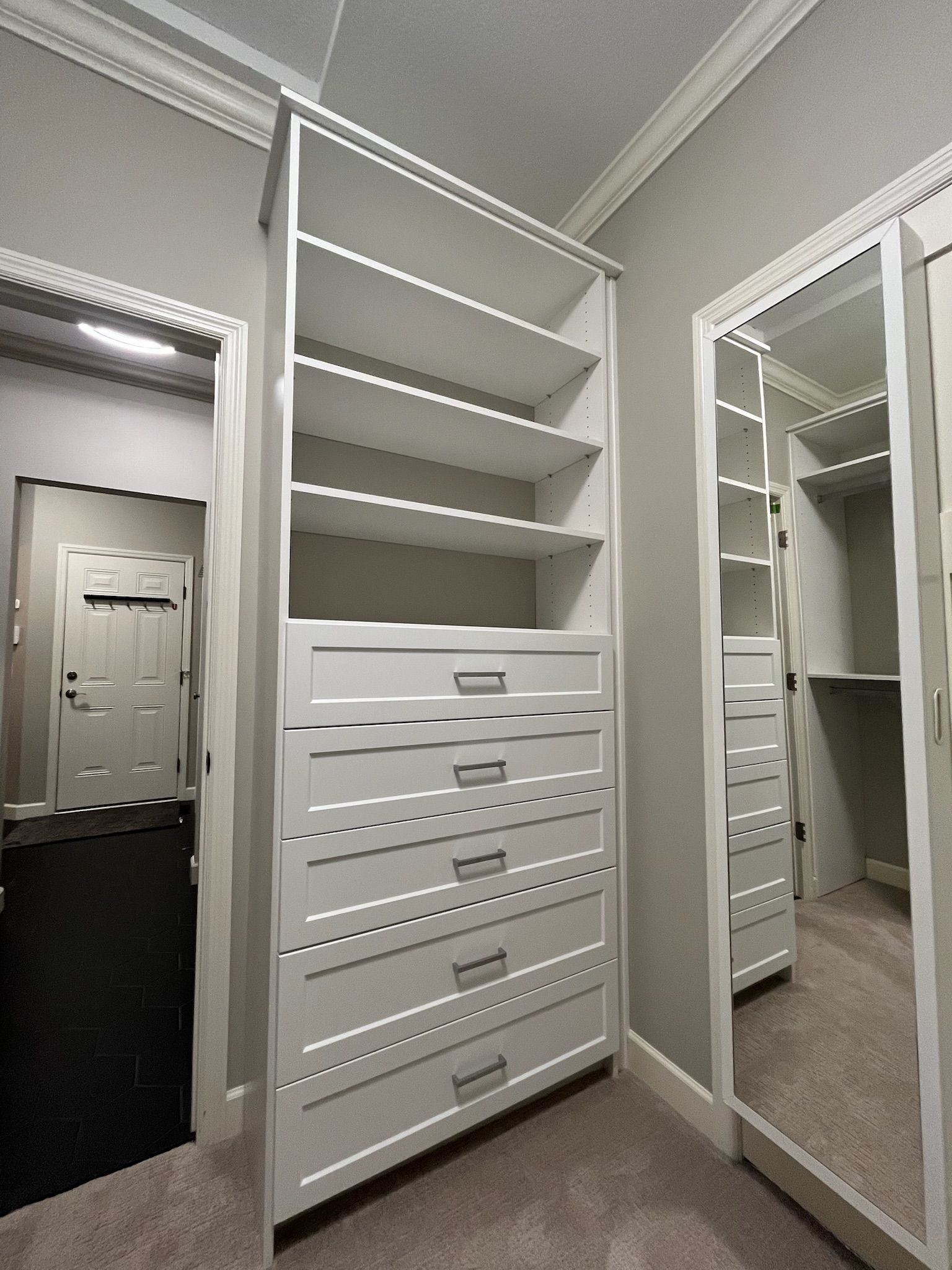 White walk-in closet with shelves, drawers, and a full-length mirror door.